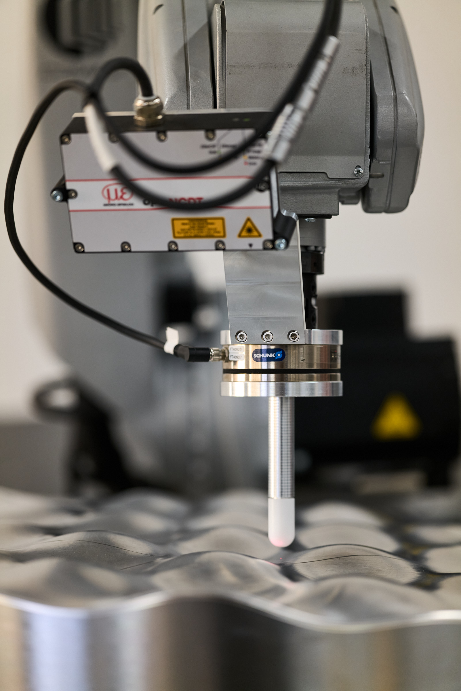 Robot arm with a laser distance sensor and a force-torque sensor approaches a curved aluminium surface.